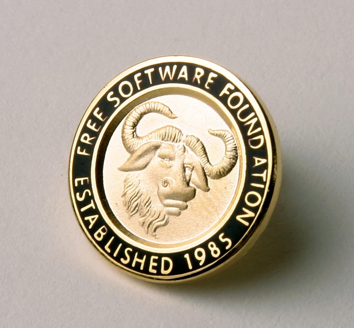 A golden GNU head pin, with text in surrounding black enamel saying "Free Software Foundation Established 1985