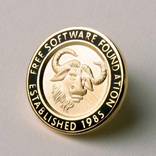 A golden GNU head pin, with text in surrounding black enamel saying "Free Software Foundation Established 1985